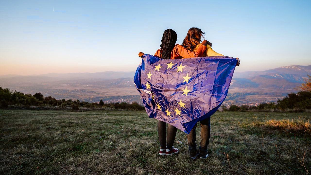 Due ragazze avvolte nella bandiera europea guardano il paesaggio